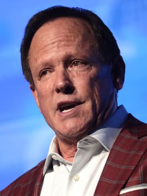 A cropped portrait of Jeff Webb, in a suit, publicly speaking