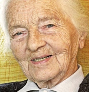 Colour Press headshot of an elderly, half-smiling woman with blue-grey eyes and white hair brushed back.